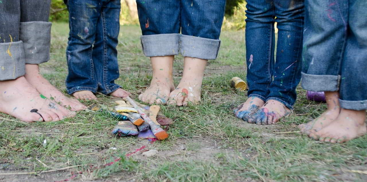 Pies de niños manchados de pintura sobre la hierba. Pinceles sucios en el suelo